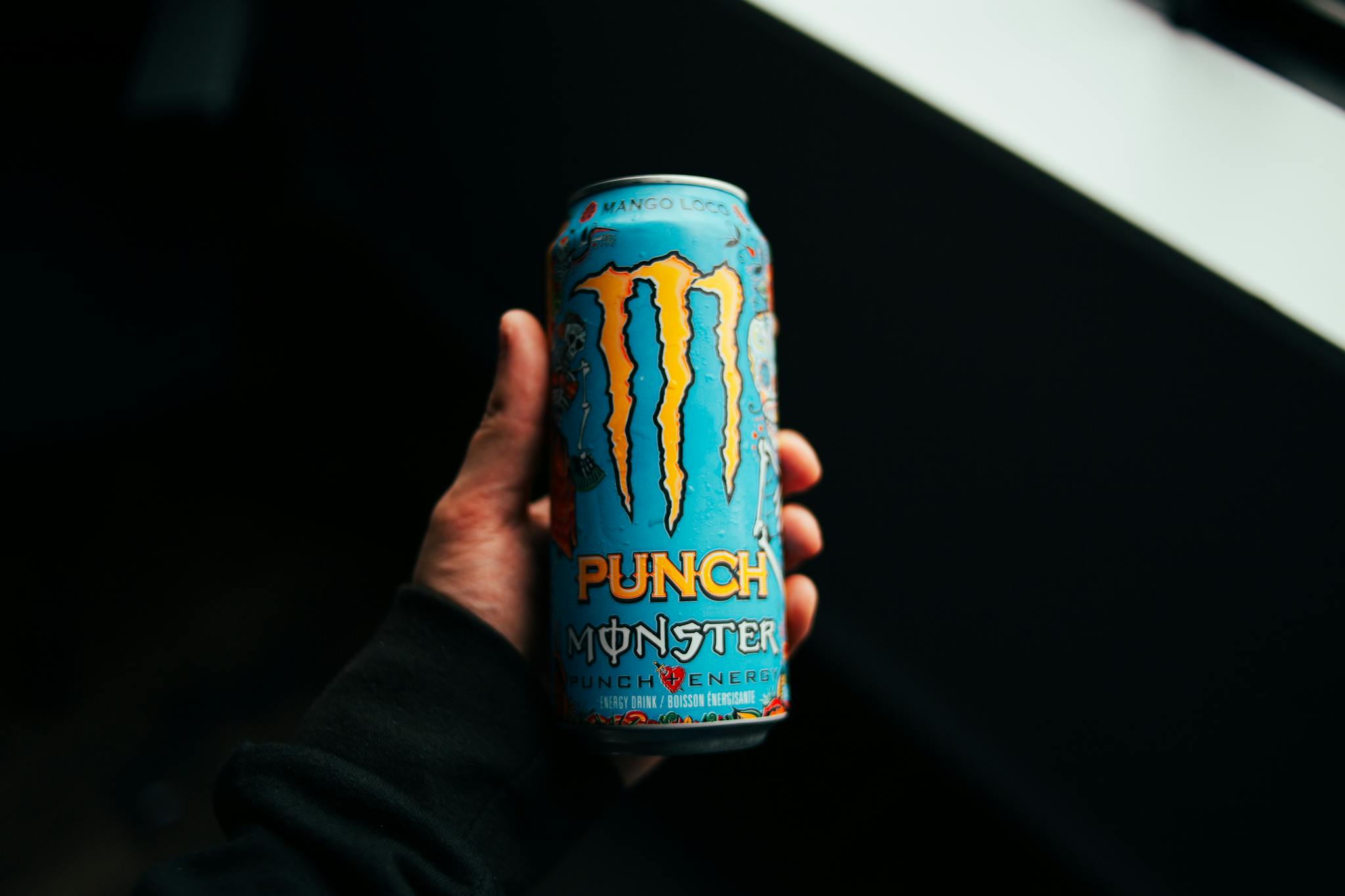 A close-up shot of a hand holding a Monster Punch energy drink can with a dark background.