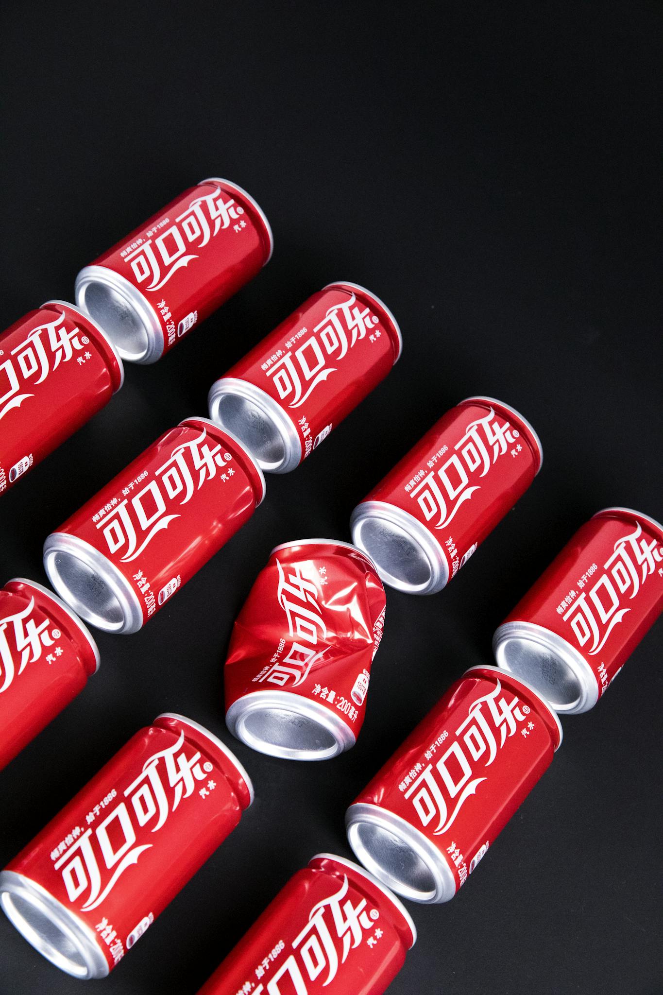 From above of red metal cans of fizzy cola placed on black table