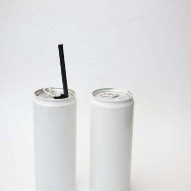 Two white beverage cans, one with a straw, on a plain background - perfect for mockup designs.